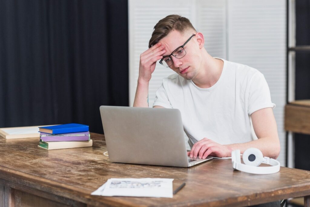worried young man looking laptop wooden table 1